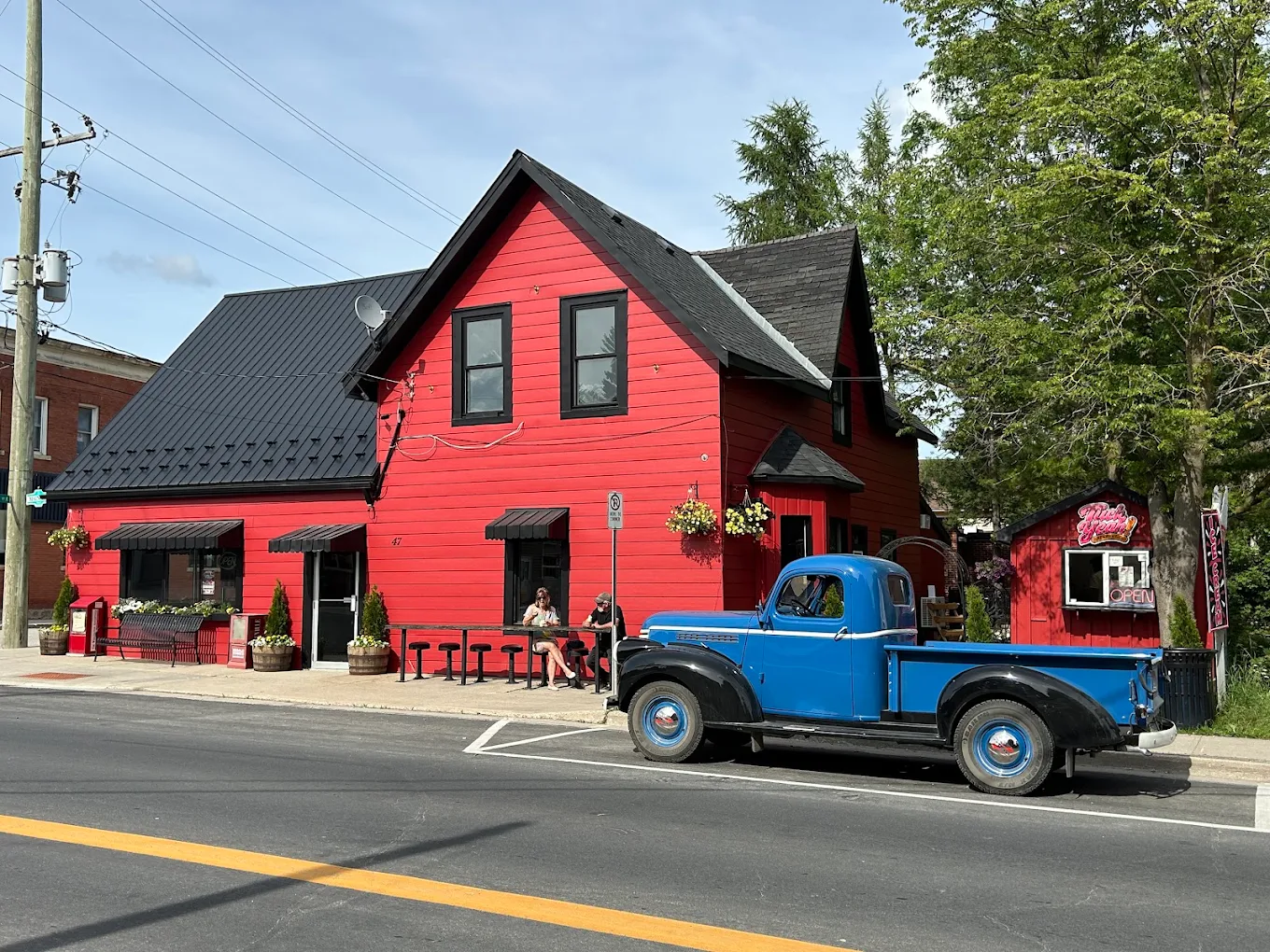 The red 1870 building on Main Street South in Grand Valley, with a vintage blue pickup truck parked out front and the Tuck Yeah! Creamery shack alongside.